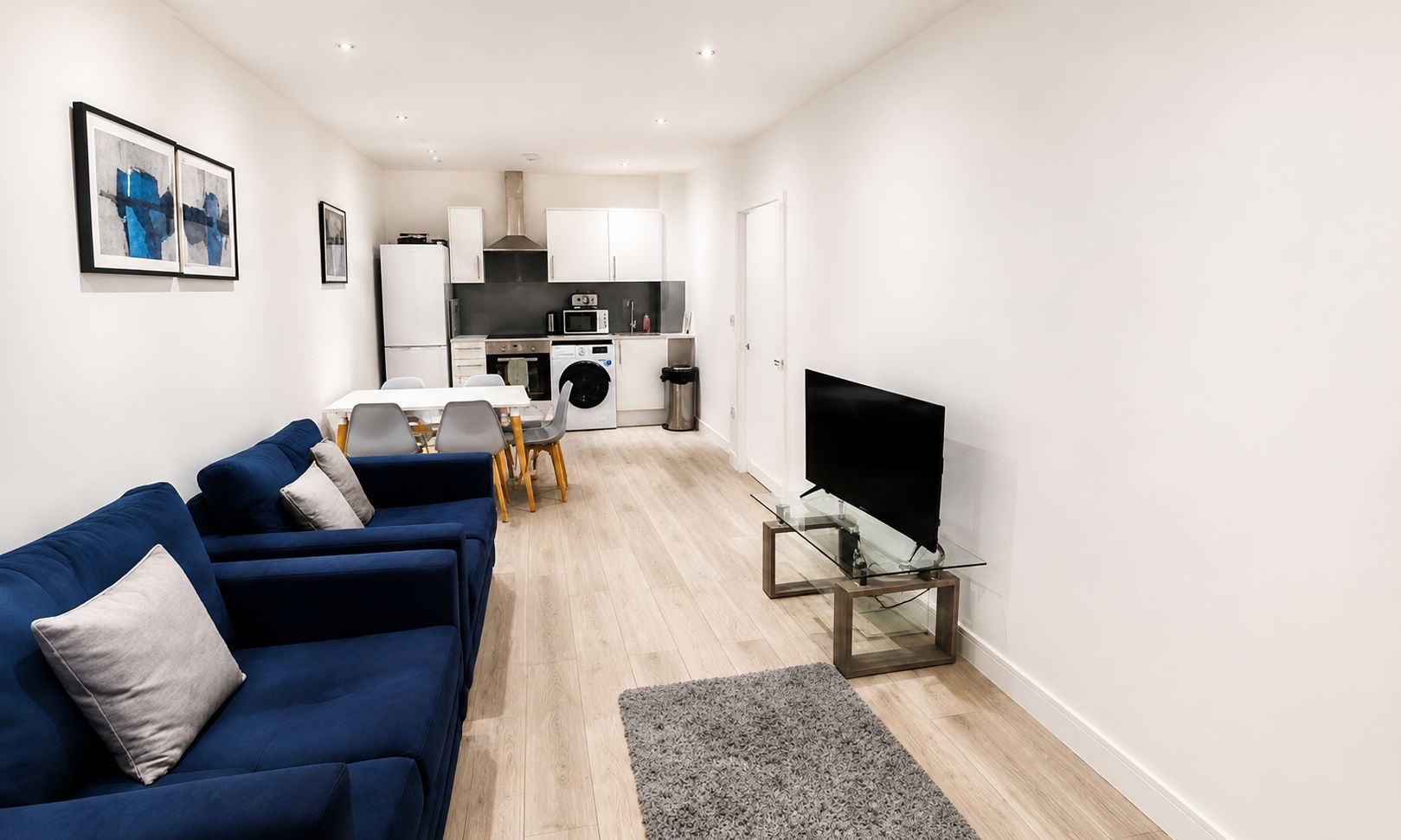A modern living room with a blue sofa, a glass coffee table, and a flat-screen TV.