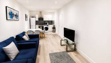 A modern living room with a blue sofa, a glass coffee table, and a flat-screen TV.