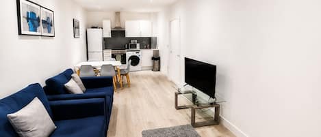 A modern living room with a blue sofa, a glass coffee table, and a flat-screen TV.
