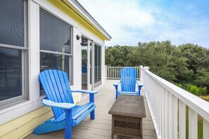 Een overdekt buitengebied met twee blauwe Adirondack-stoelen en een klein rieten tafeltje.