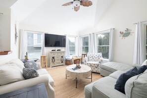 A spacious living room with a large flat-screen TV, two sofas, a coffee table, and a ceiling fan. - Golf Views, Private Pool/Spa, Community Amenities! (Corolla)