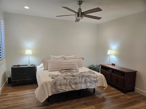 A bedroom with a bed, bedside lamps, a ceiling fan, a wooden dresser, and a nightstand. - Spacious 3-bedroom condo in tranquil Rancho Mirage (Rancho Mirage)