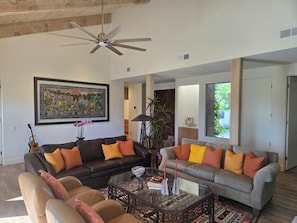 A living room with two sofas, a coffee table, a ceiling fan, and a large framed artwork. - Spacious 3-bedroom condo in tranquil Rancho Mirage (Rancho Mirage)