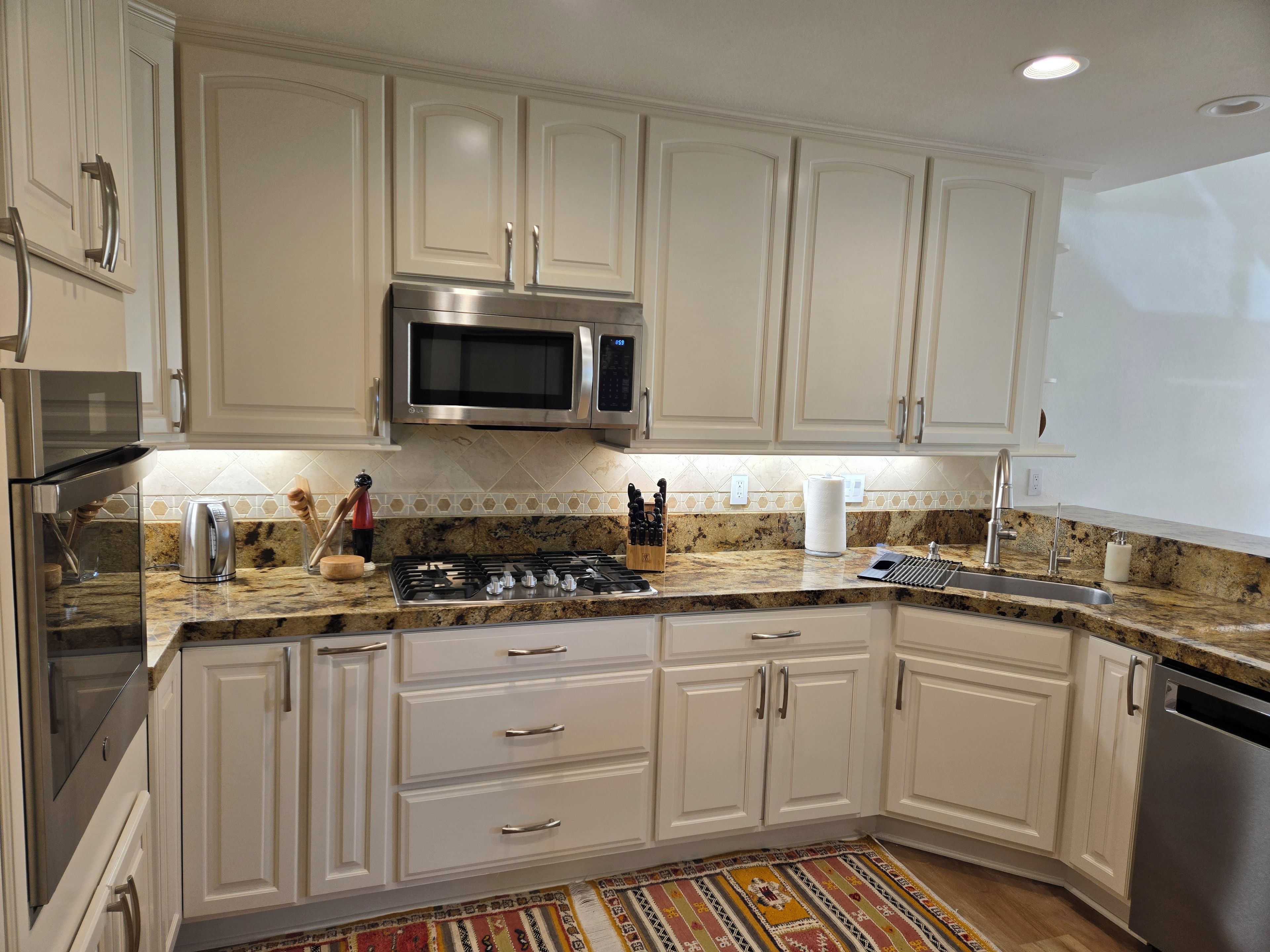 A kitchen with white cabinets, a stainless steel microwave, a gas stove, and a granite countertop.