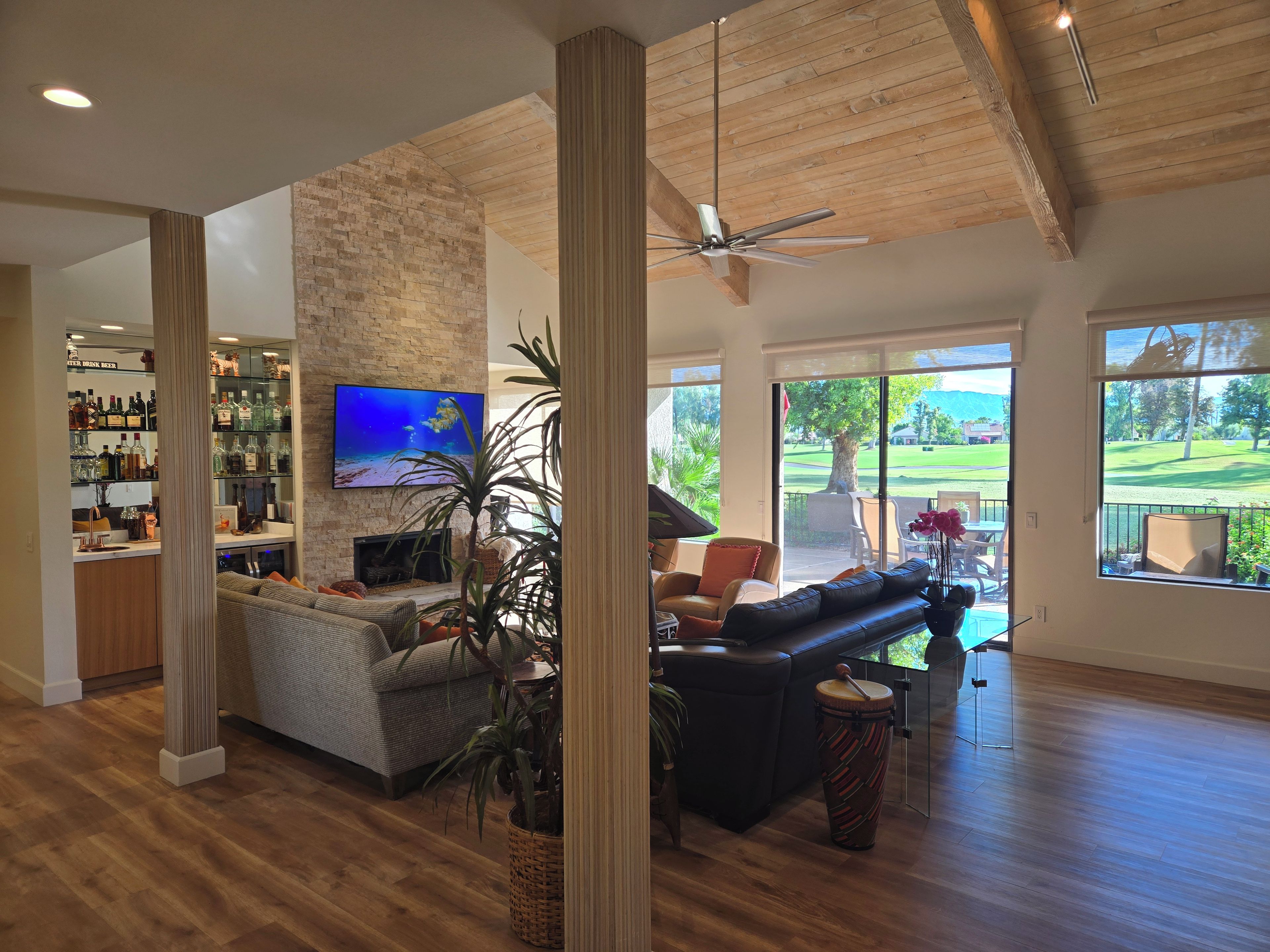 A spacious living area with a fireplace, comfortable seating, a television, and a view of a golf course through large windows.