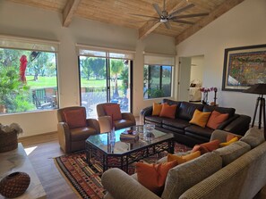 A spacious living room with a large window, a ceiling fan, and a view of the outdoors. - Spacious 3-bedroom condo in tranquil Rancho Mirage (Rancho Mirage)
