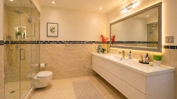 Un baño moderno con ducha de vidrio, inodoro, tocador con un espejo grande y una planta decorativa.