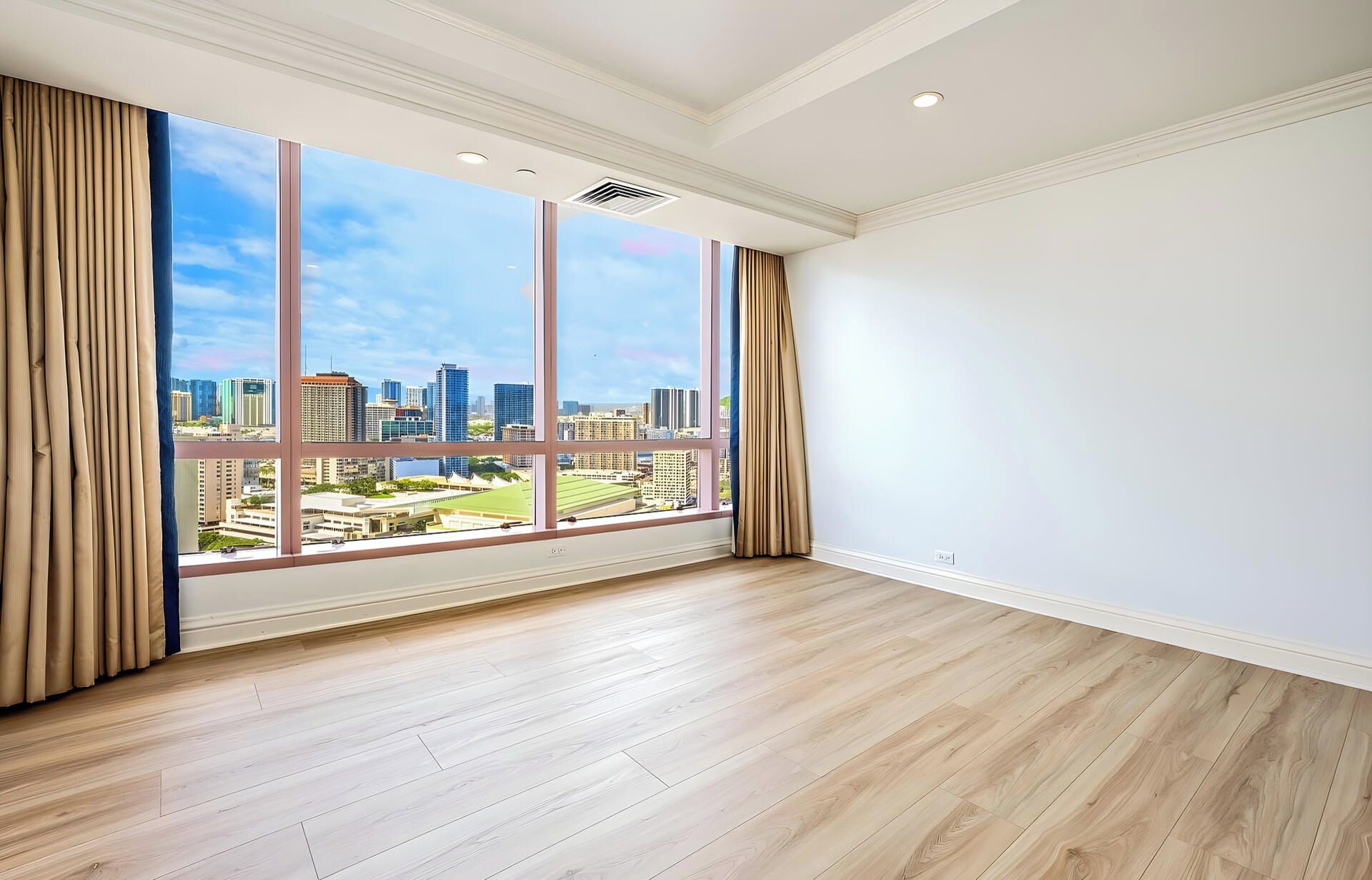 A room with large windows, wooden flooring, and a view of a cityscape.