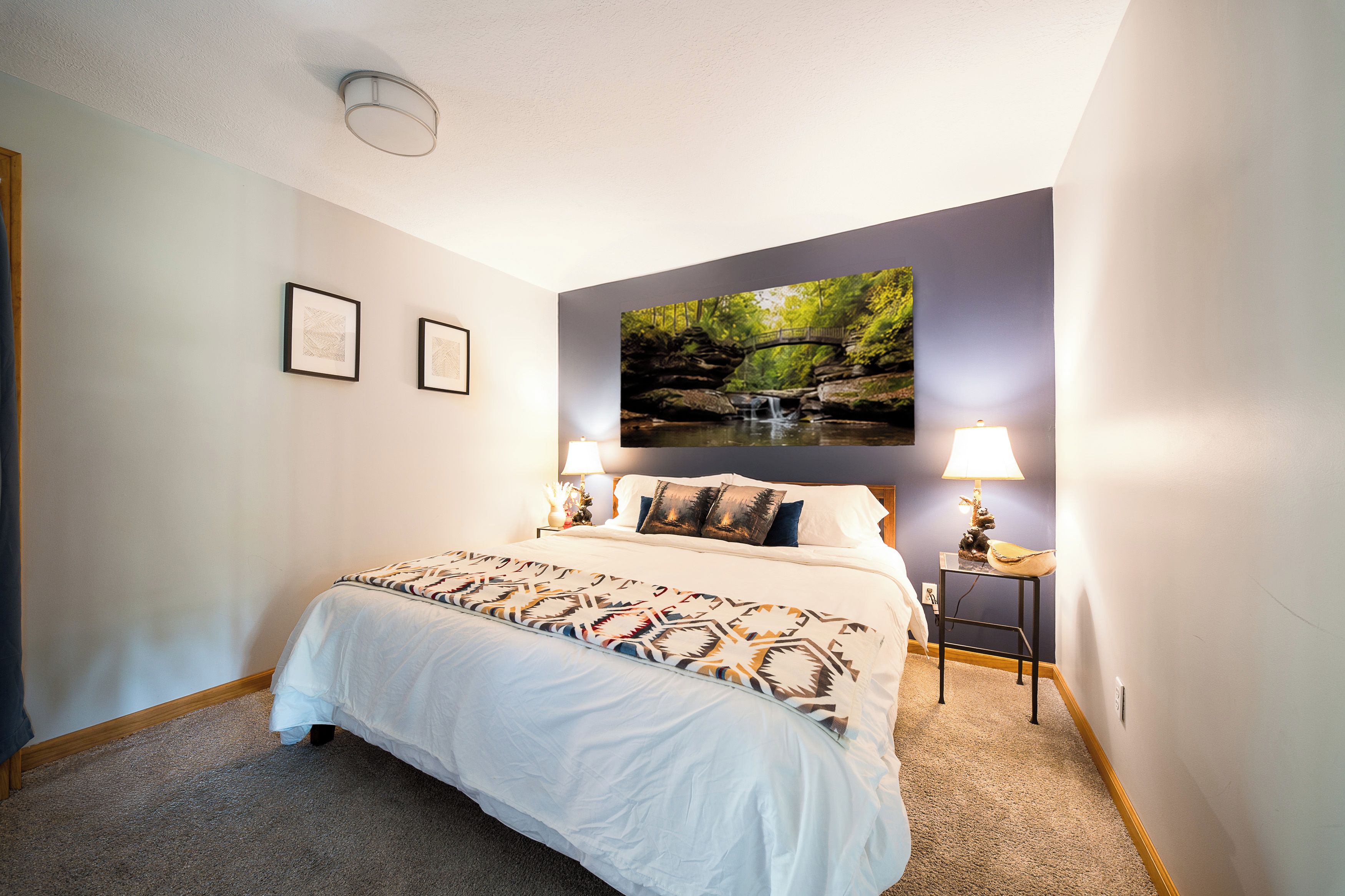 Un dormitorio con cama, mesita de noche, un cuadro en la pared y lámpara del techo.