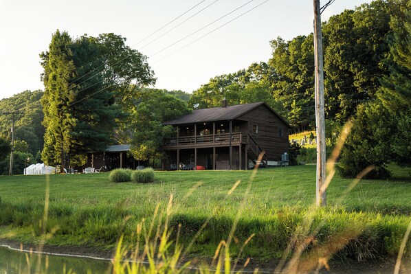 A wooden cabin with a porch, surrounded by a grassy field and trees.