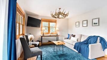 Ein Wohnzimmer mit einer Couch, einem Sessel, einem Couchtisch, einem Fernseher, einer Chandelieber und Kunstwerken an der Wand.