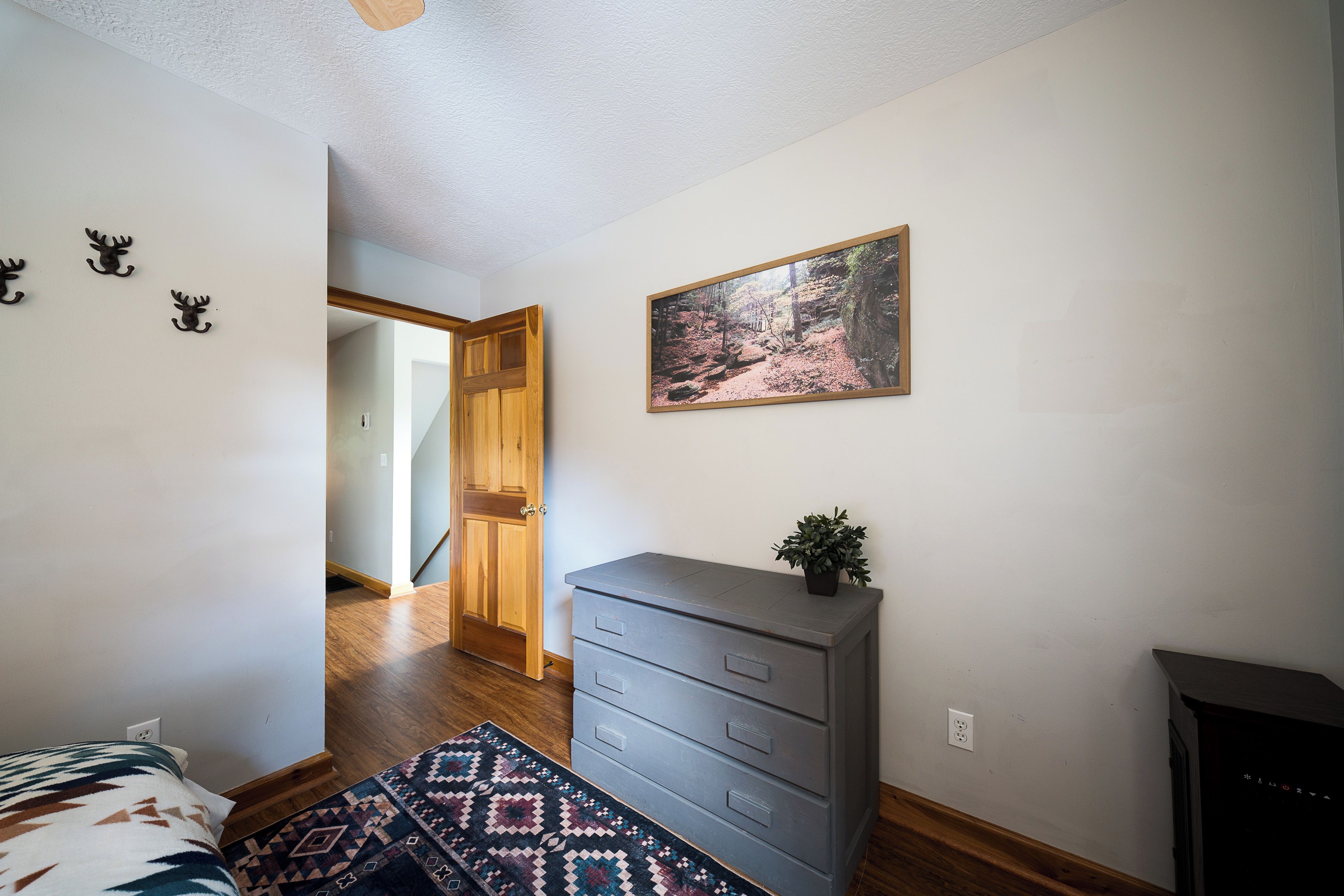 Une chambre à coucher avec un lit, une commode, un tapis, un tableau et un couloir menant à une autre pièce.