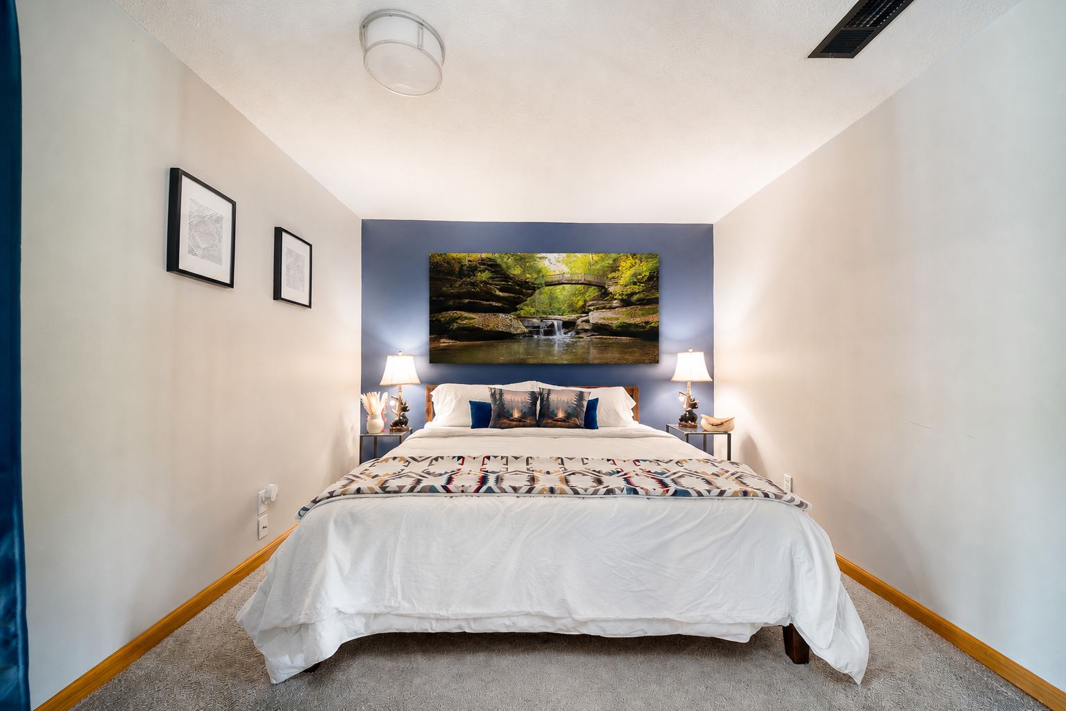 Ein Schlafzimmer mit einem Bett, zwei Nachttischlampen, einem an der Wand befestigten Fernseher und gerahmten Bildern.
