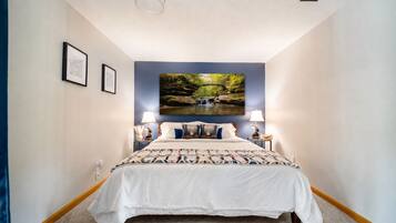 Ein Schlafzimmer mit einem Bett, zwei Nachttischlampen, einem an der Wand befestigten Fernseher und gerahmten Bildern.