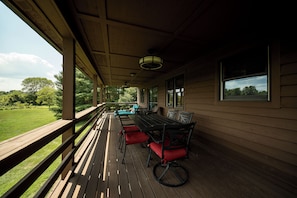 A covered outdoor deck with a table and chairs, overlooking a grassy area.