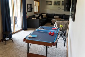 A ping pong table in a living room with a sofa and a small table with a vase of flowers.