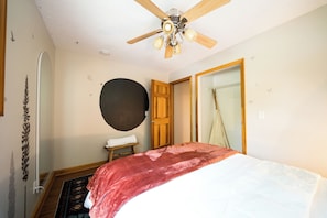 A bedroom with a bed, a ceiling fan, a wooden door, and a large mirror.