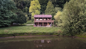 Uma cabana de dois andares com varanda, localizada à beira de um lago com reflexo.