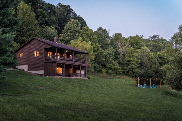 A wooden cabin with a balcony, surrounded by a grassy landscape and dense trees.