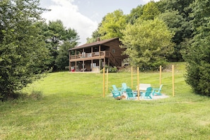 A wooden cabin with a balcony, surrounded by a grassy area and trees.