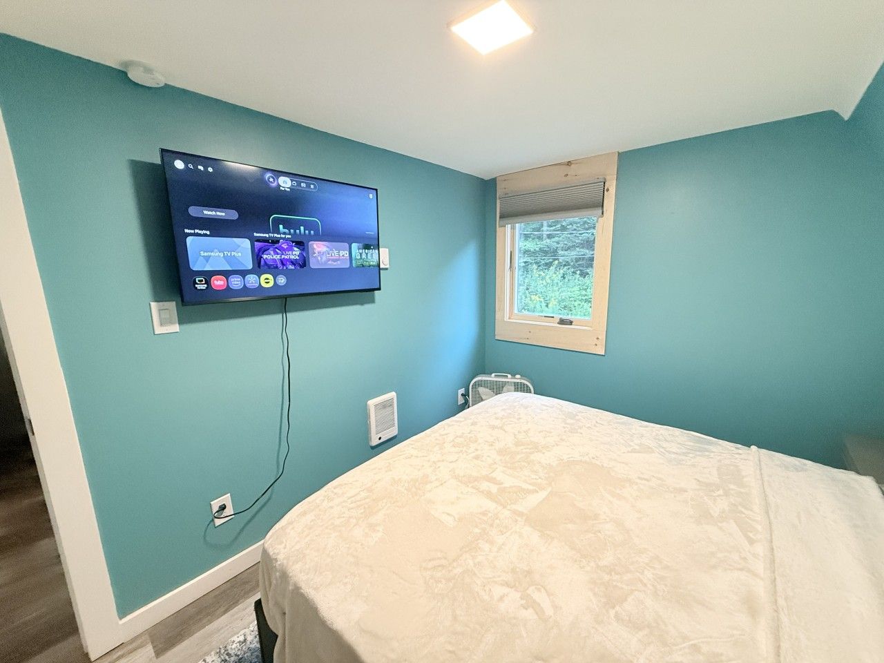 Une chambre à coucher avec un lit, un téléviseur fixé au mur et une fenêtre avec des stores.