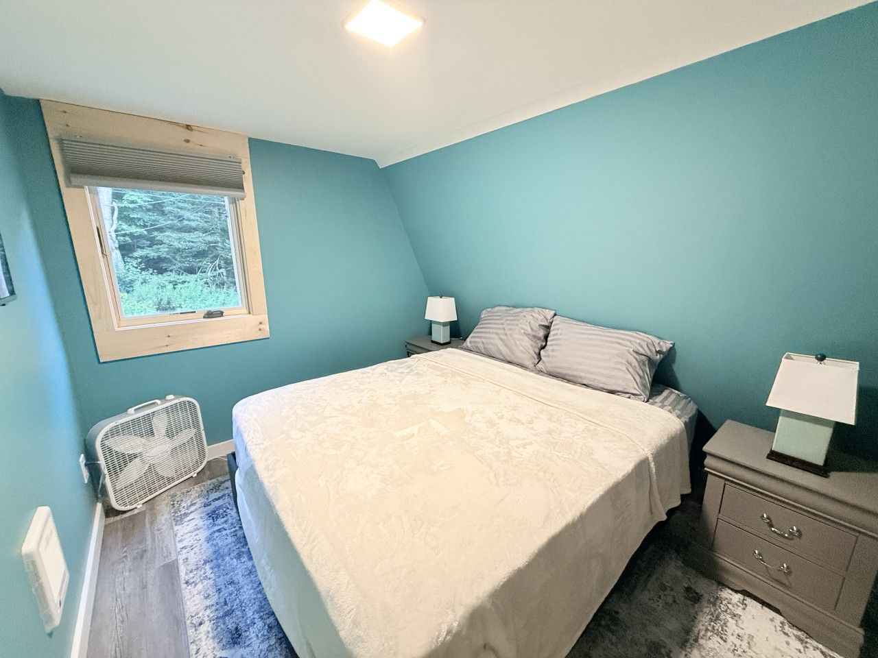 A bedroom with a bed, bedside tables, a window, and a radiator.