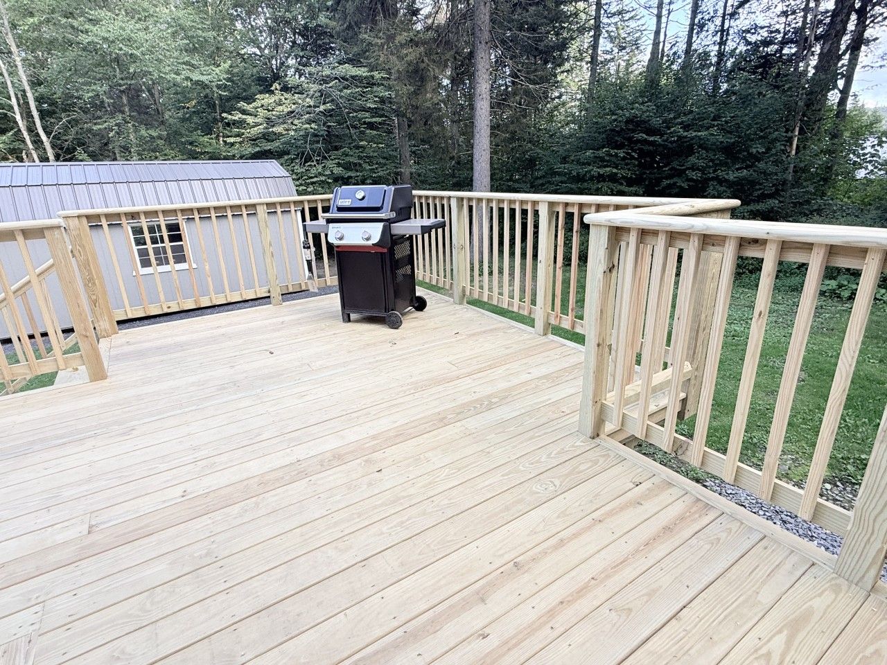 Een houten terras met een barbecue en een kleine schuur.