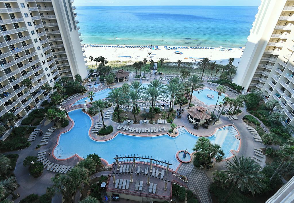 A resort with a central swimming pool, palm trees, and a beach view.