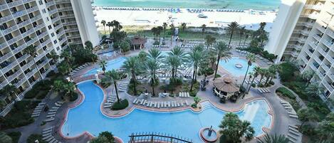 A resort with a central swimming pool, palm trees, and a beach view.