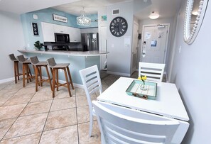 A kitchen with a central island, bar stools, and a dining table with chairs. - Shores Of Panama #1215 Paradise awaits! Stunning Beach views! (Panama City Beach)