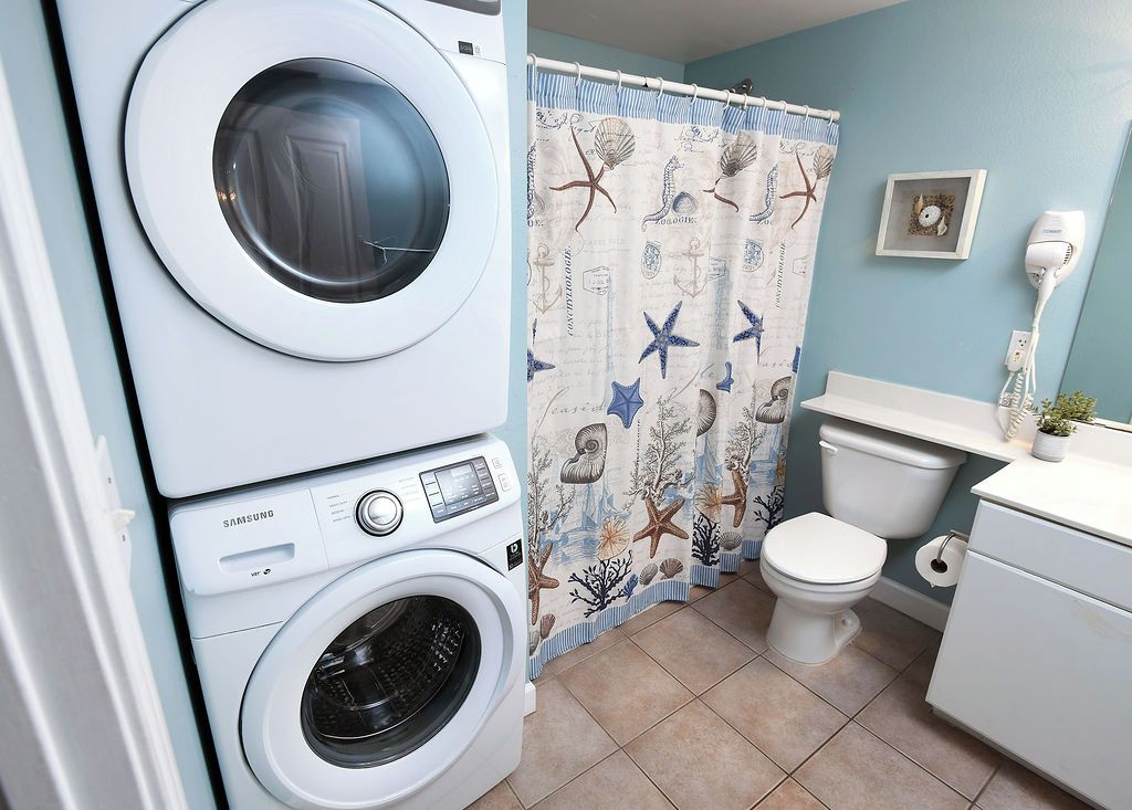 A laundry area with a Samsung washer and dryer, a toilet, and a shower curtain with a nautical theme.