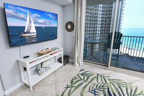 A living room with a flat-screen TV, a white console table, a patterned rug, and a balcony with a glass door overlooking the ocean. - Shores Of Panama #1215 Paradise awaits! Stunning Beach views! (Panama City Beach)