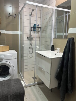 Uma casa de banho moderna com cabine de duche em vidro, máquina de lavar roupa embutida e lavatório com porta-toalhas.