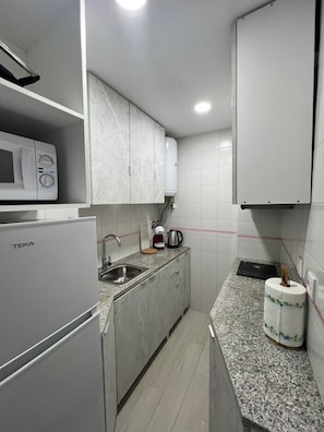 Cozinha compacta com micro-ondas, pia e chaleira no balcão.