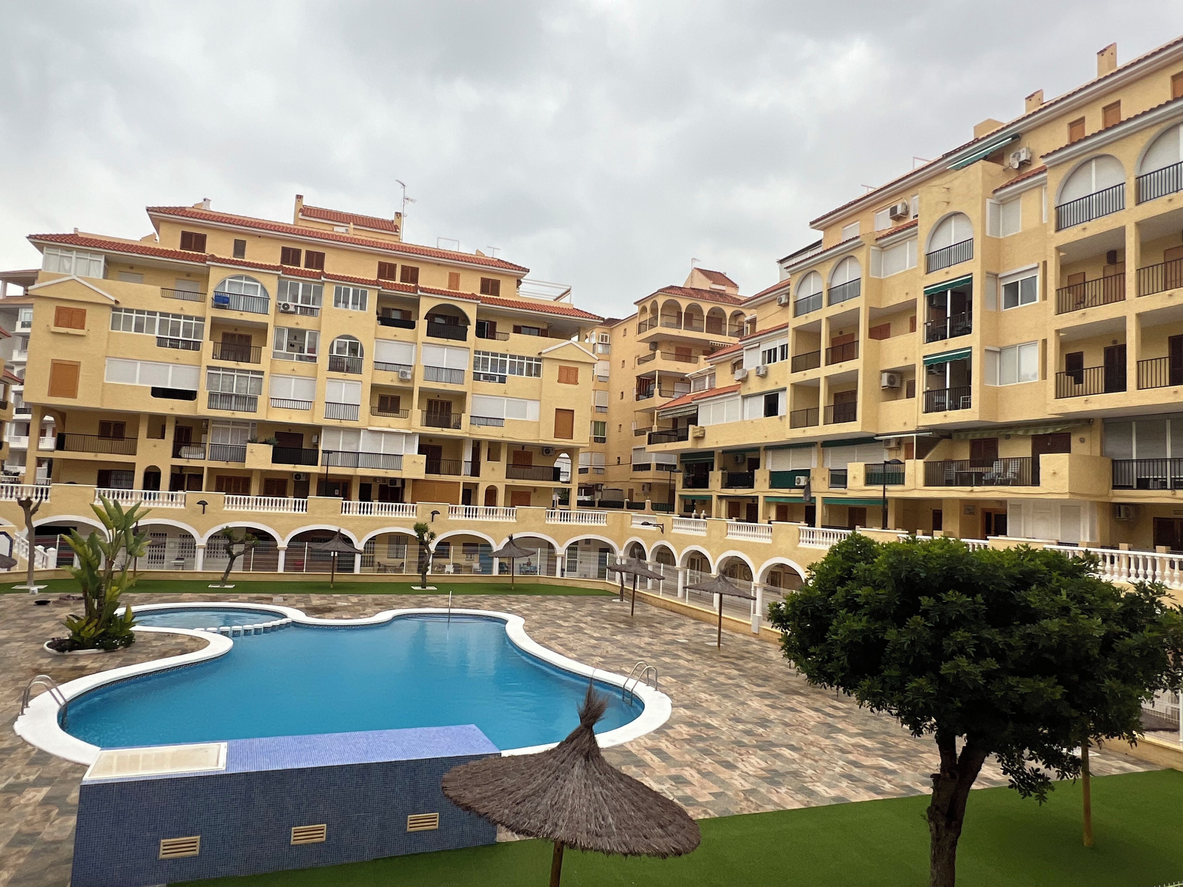 Une cour d’hôtel avec une piscine, plusieurs balcons et une allée dallée.