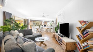 Un salon moderne avec un canapé, une table basse et un téléviseur. Il y a également un coin cuisine avec une table et des chaises, ainsi qu'une bibliothèque remplie de livres.