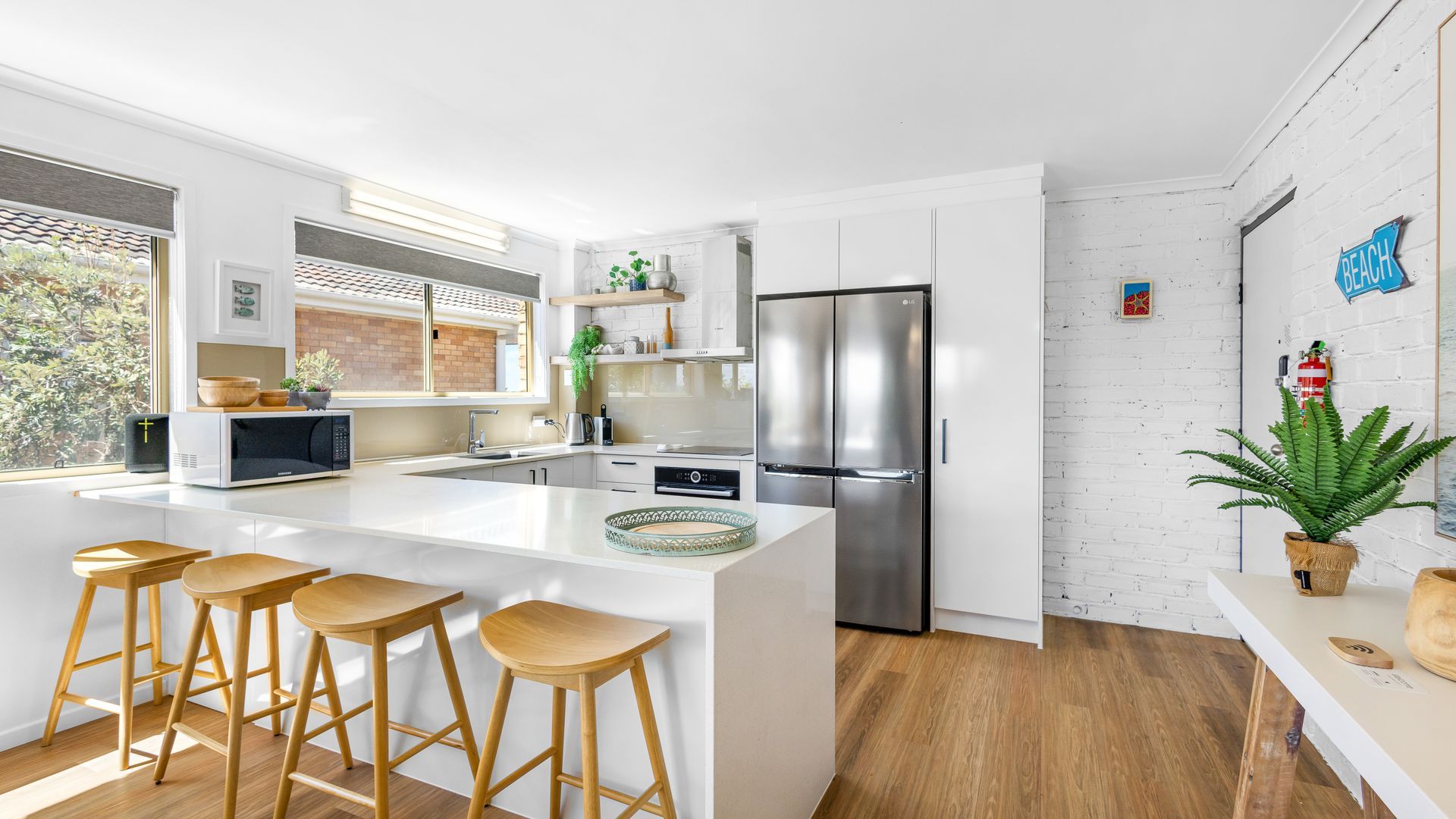 Una cocina moderna con una isla grande, taburetes de bar, un refrigerador de acero inoxidable y una pared de ladrillo.