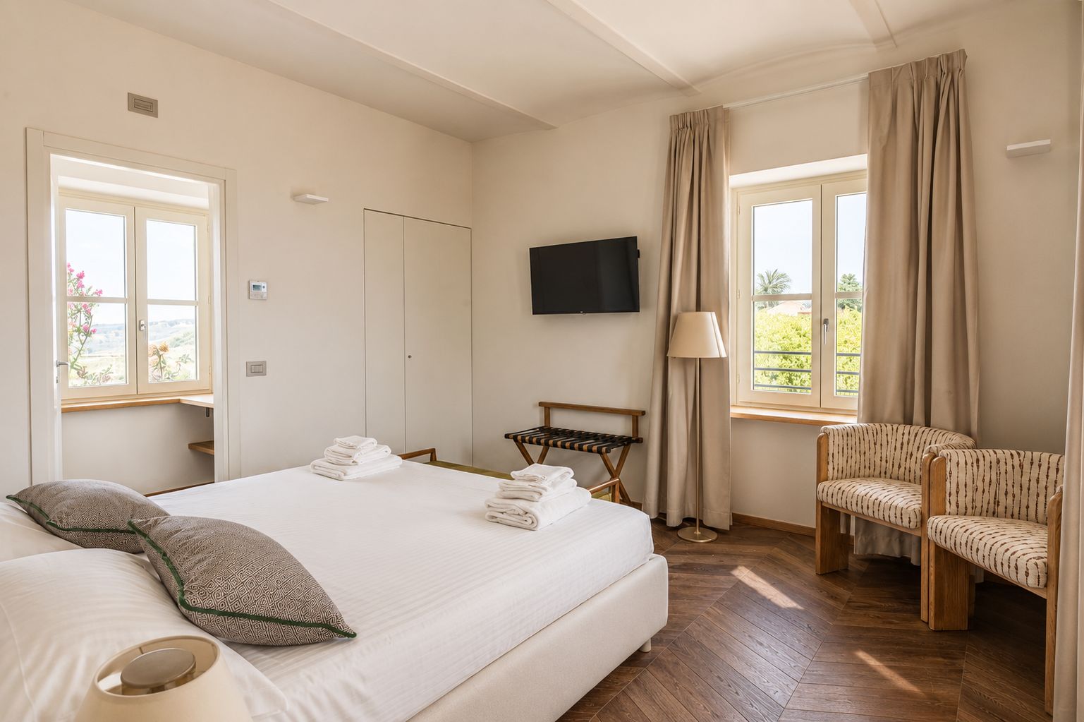 Ein Hotelzimmer mit einem Bett, einem Fernseher, einem Sessel, einer Lampe und einem Fenster mit Vorhängen.