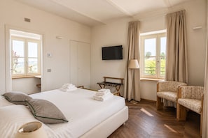 A hotel room with a bed, a TV, a chair, a lamp, and a window with curtains.