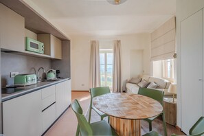 A modern kitchen with a dining area, including a round wooden table and green chairs. - Bricco Neri - Alba - One Bedroom Apartment, Sleeps 4 (Rodello)