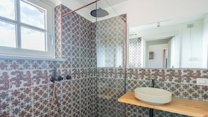 Een badkamer met patroon betegelde vloer, een douchecabine met glazen wanden, een wastafel met houten aanrechtblad en een grote spiegel.
