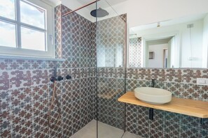 Casa de banho com azulejos estampados, cabine de duche com vidro, lavatório com bancada de madeira e um espelho grande.