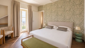 Een hotelkamer met een bed, een stoel, een tafeltje, een balkon en behang met een patroon.