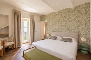 Quarto de hotel com cama, uma cadeira, uma mesa pequena, varanda e papel de parede estampado.