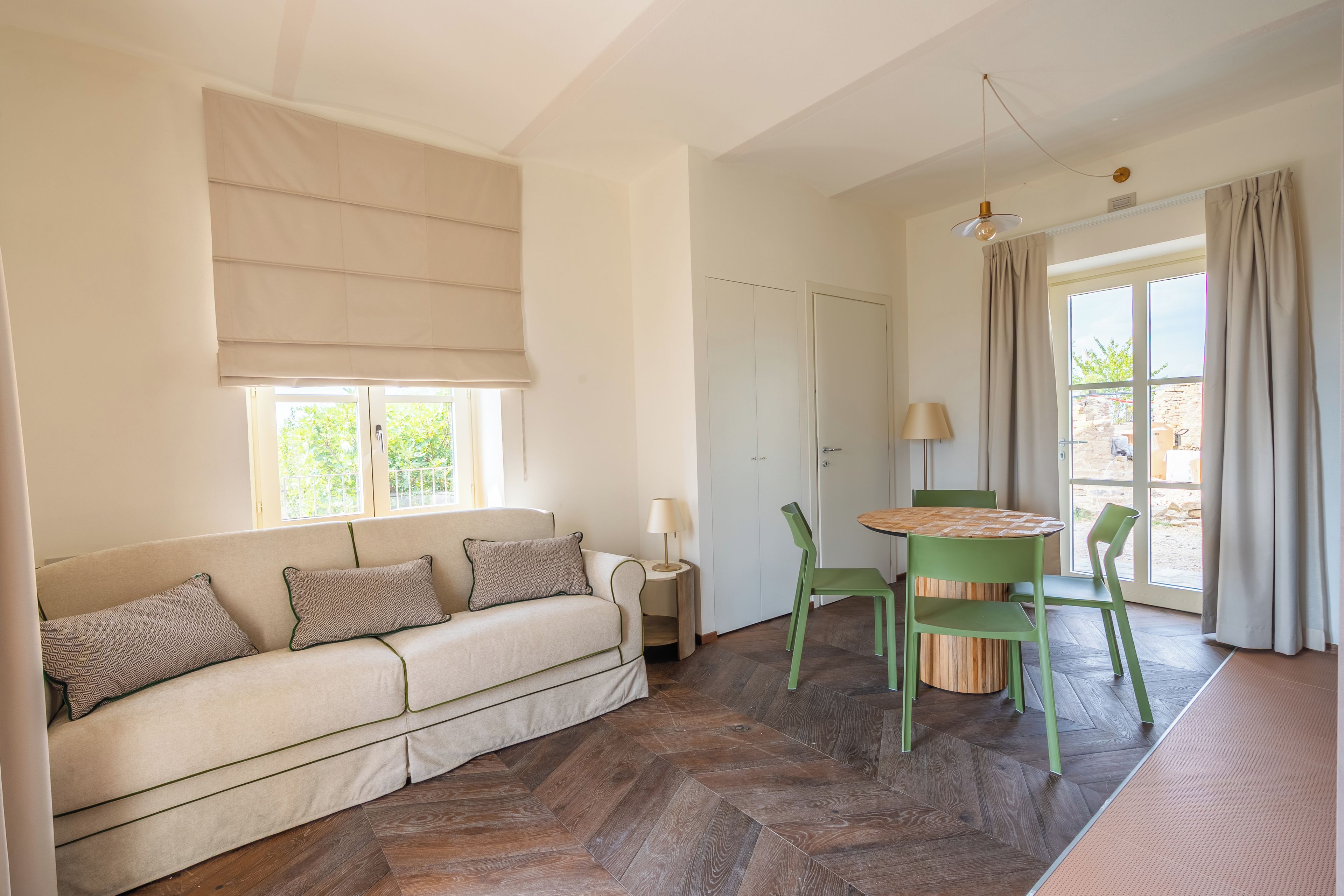 Ein Zimmer mit einer Couch, einem Tisch, Stühlen, einer Lampe und einem Vorhangfenster.