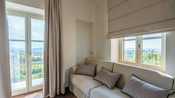 Ein Zimmer mit einer Couch, einem Fenster mit Blick auf Grünflächen und einem Vorhang.