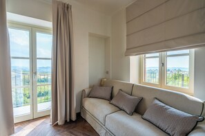 Quarto com sofá, janela com vista para o verde e cortina.