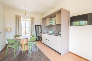 A compact kitchen with a microwave, toaster, and sink. There is a dining area with a round table and chairs. - Bricco Neri - Alba - One Bedroom Apartment, Sleeps 4 (Rodello)