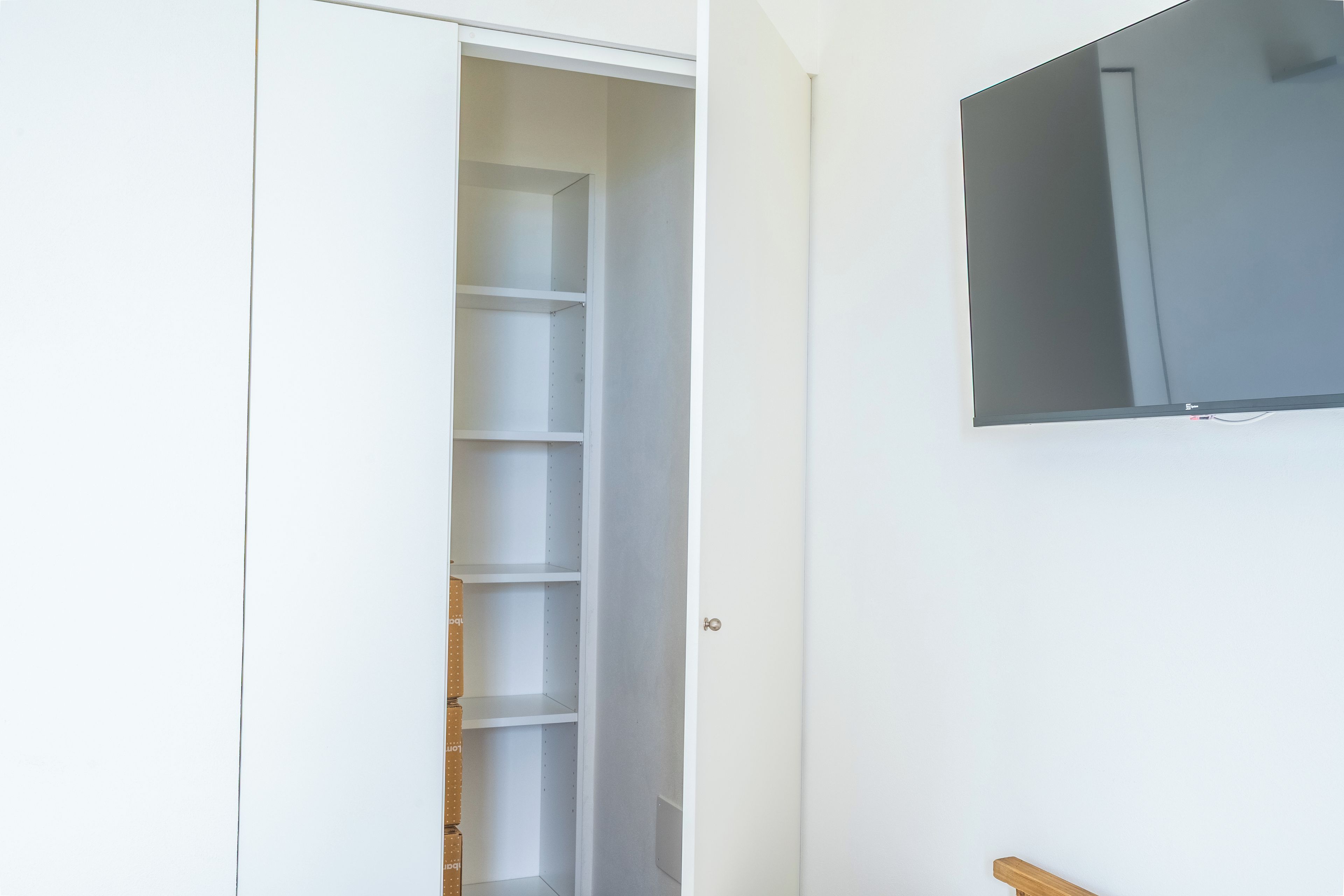 Un placard blanc avec des étagères, une porte et un téléviseur fixé au mur.