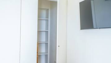 Un armadio bianco con ripiani, una porta e una TV fissata al muro.